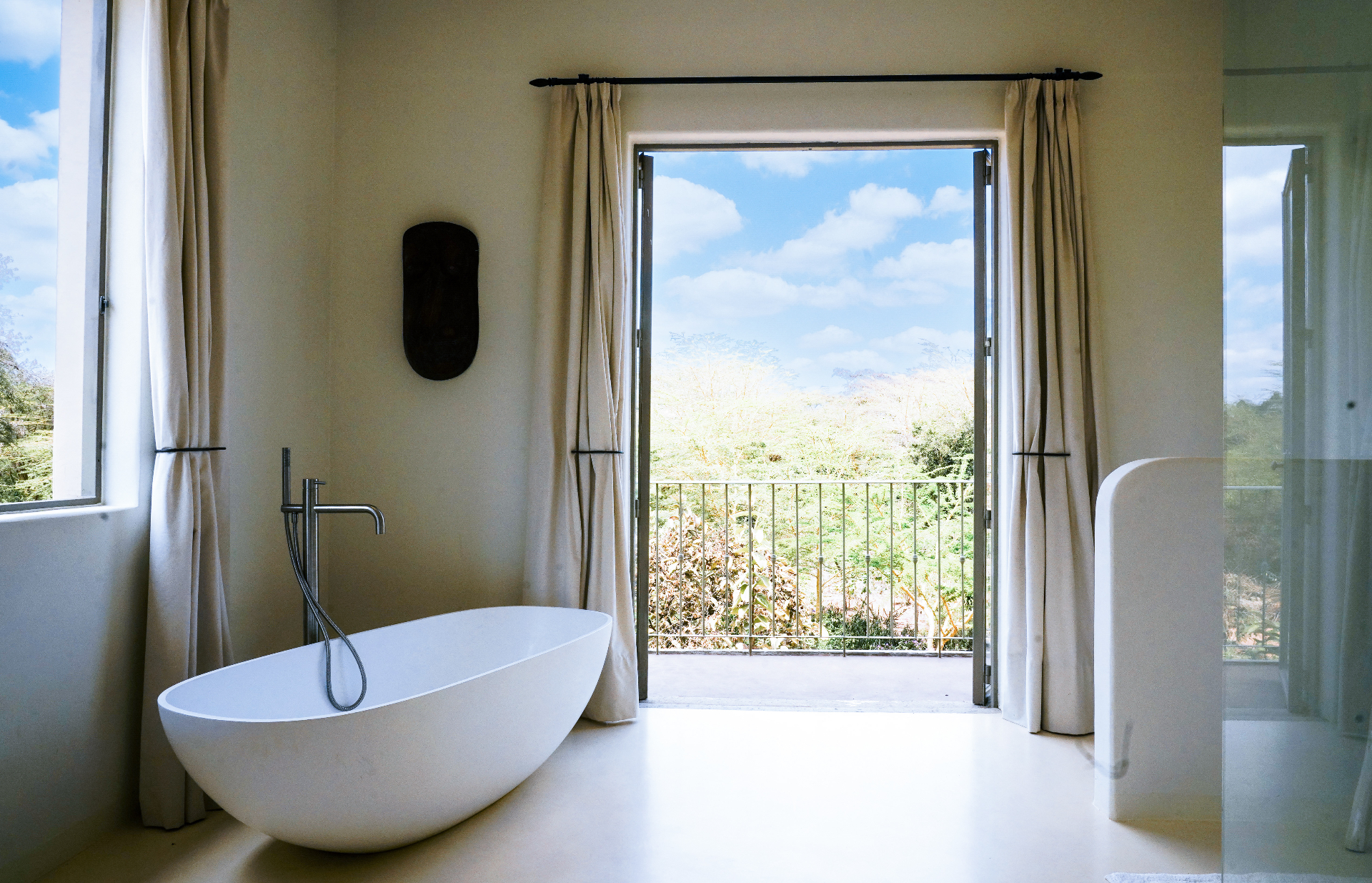 Freestanding bath with open balcony doors and acacia views