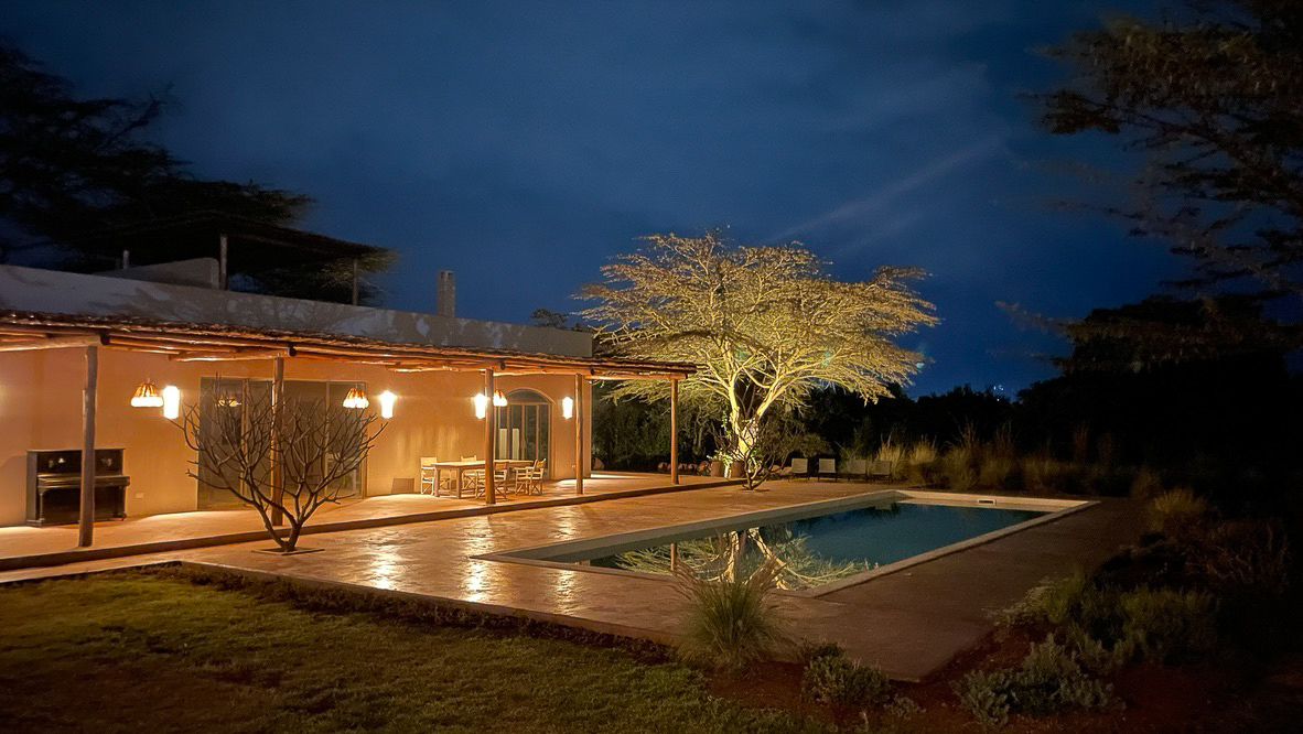 Pool House and pool lit at night with lantern-lit acacia tree