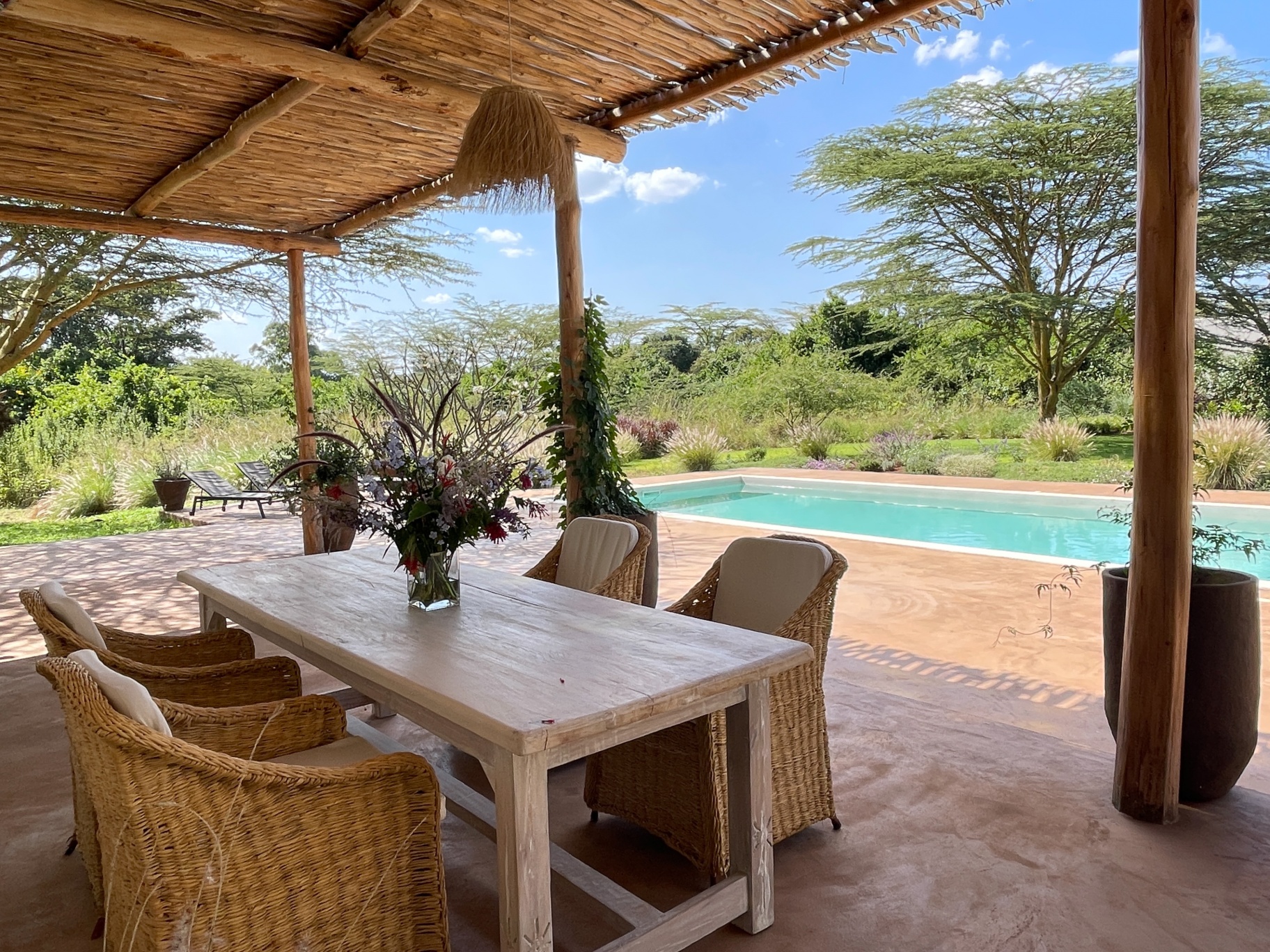 Veranda dining table under a makuti roof beside the pool